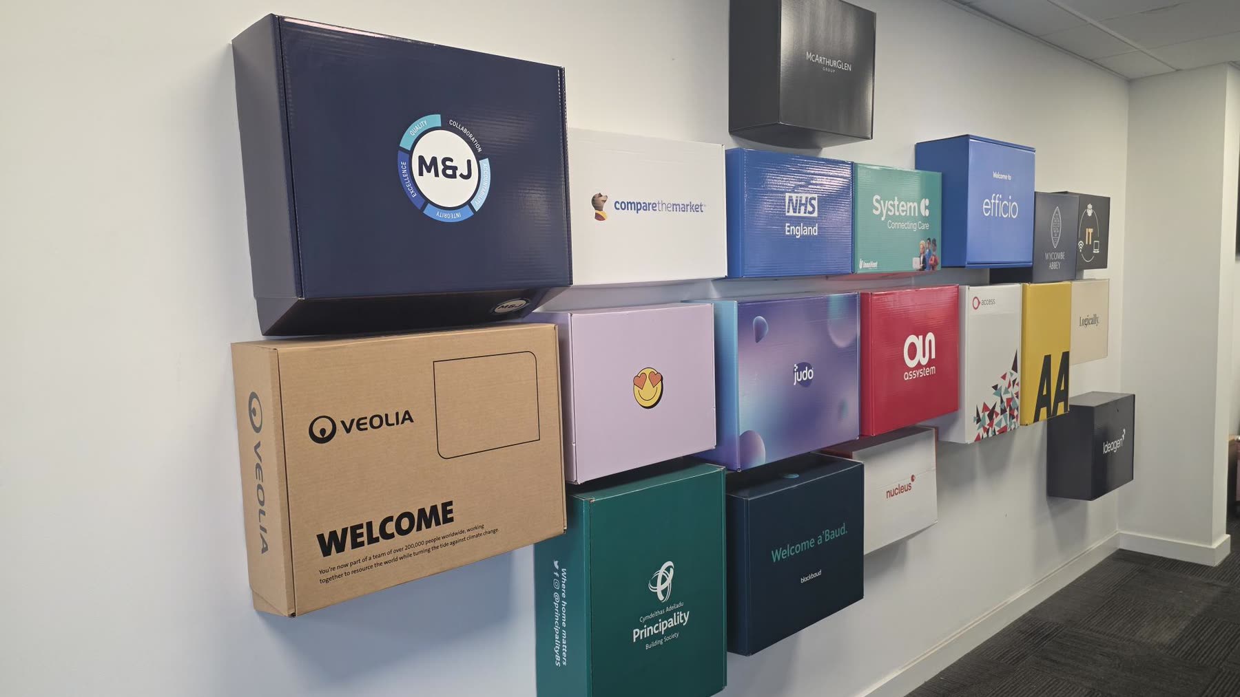 The welcome box wall at GreensafeIT — dozens of bespoke new-starter boxes, each printed in a different customer's brand