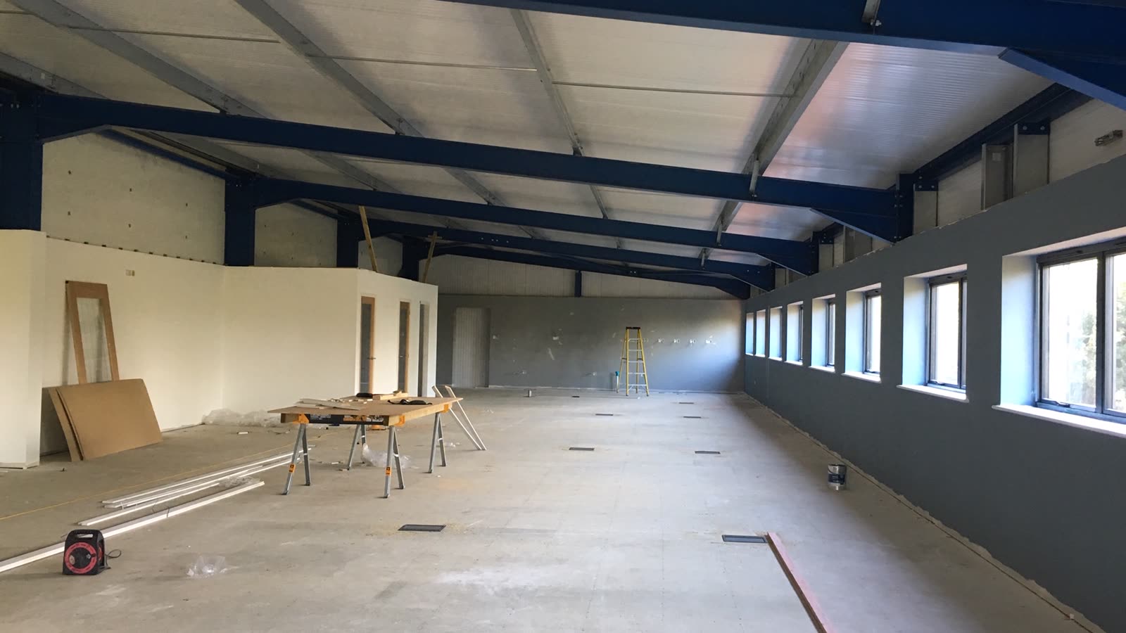 A bare office shell — exposed steel roof frame, unpainted partition walls and a concrete floor