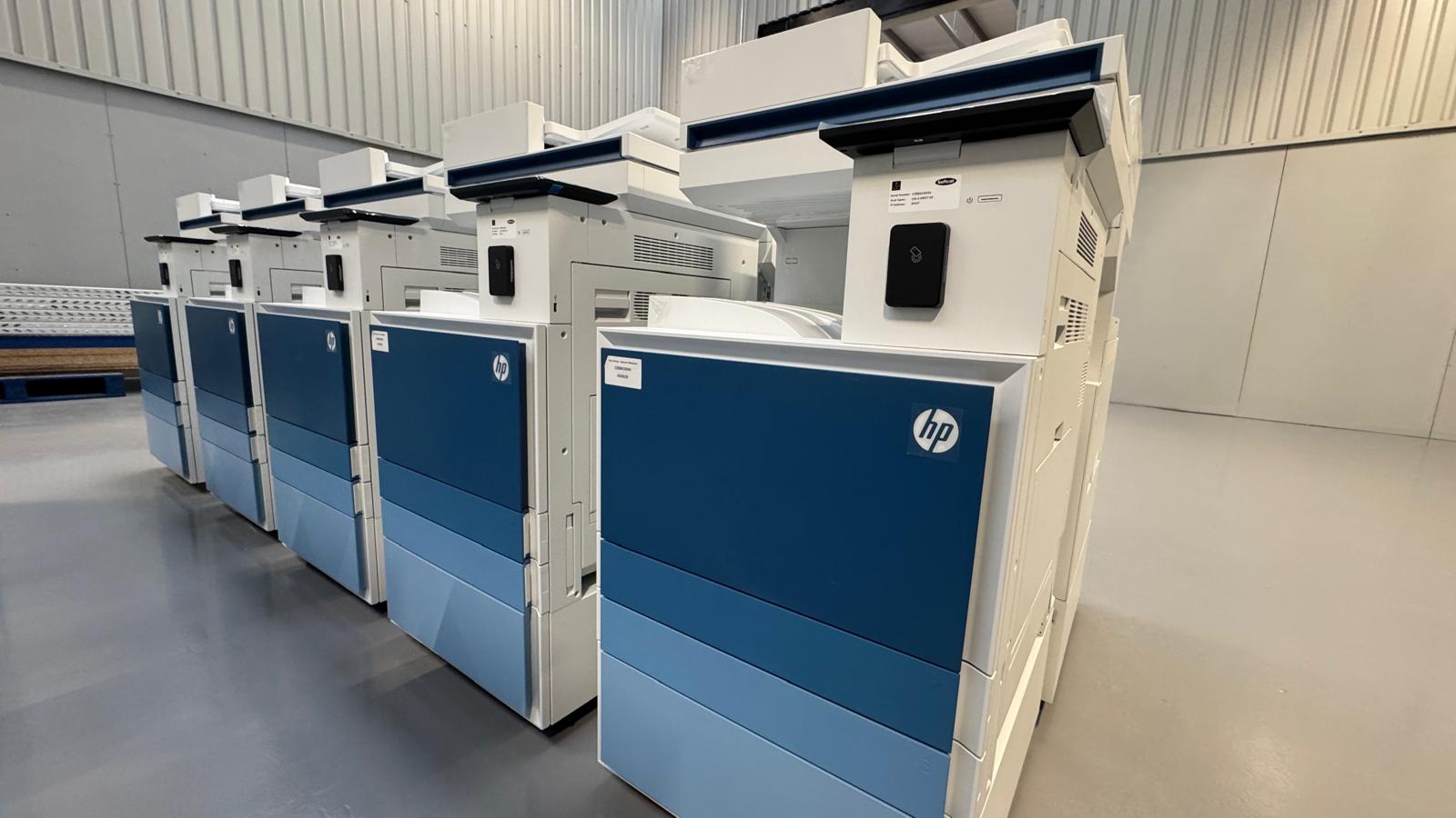 Multifunction printers lined up in the warehouse, each with its own asset label, ready for a wave release