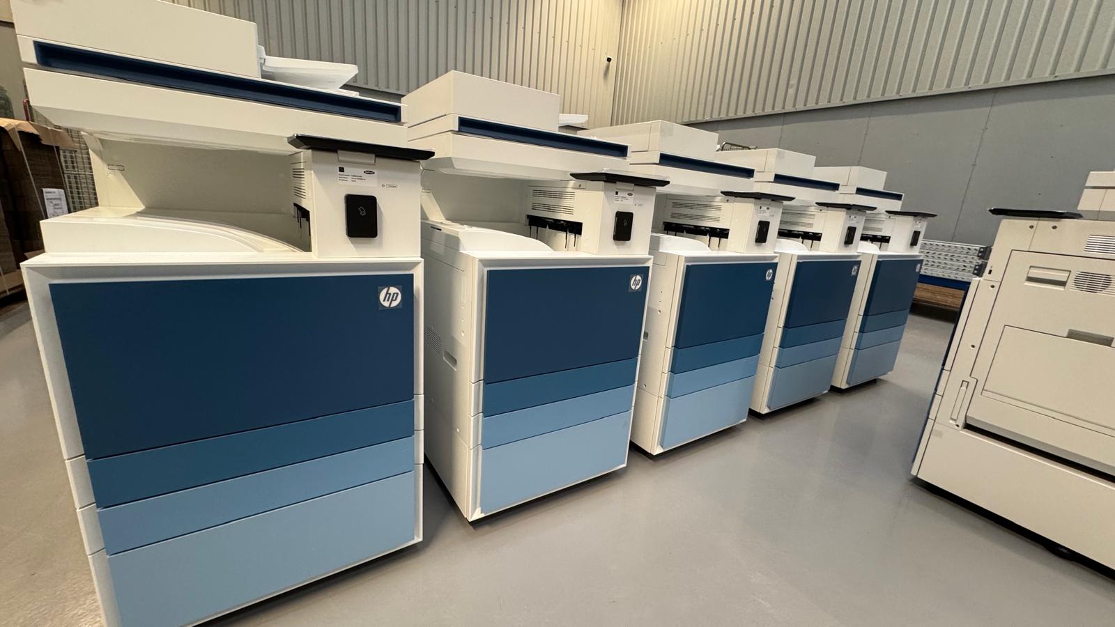 A row of new multifunction printers, labelled and staged in the Greensafe warehouse before deployment