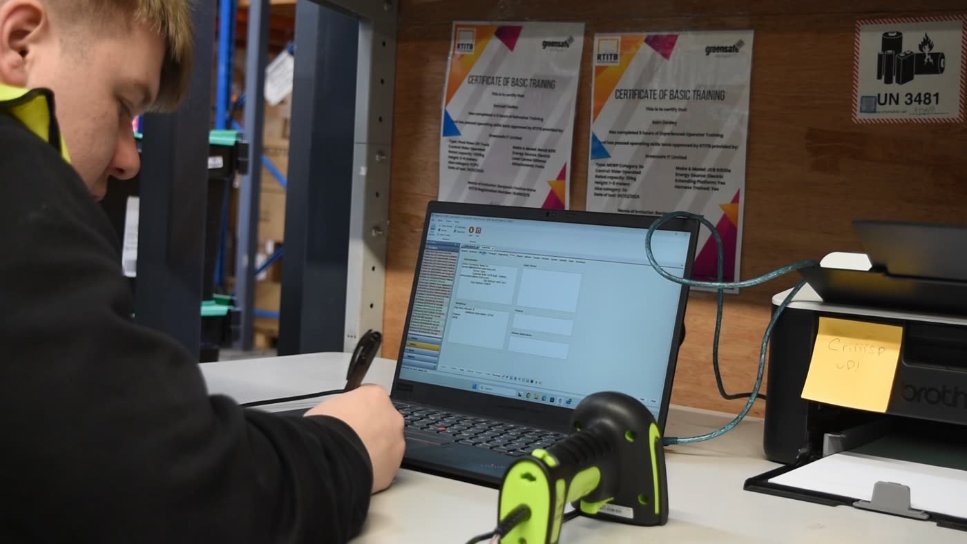 Warehouse operative booking stock in at a laptop with a handheld barcode scanner