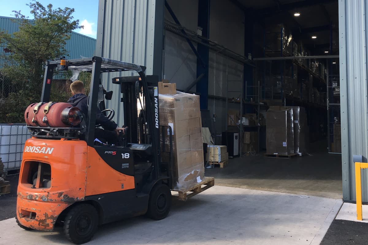 A forklift carrying a wrapped pallet in through the warehouse loading door