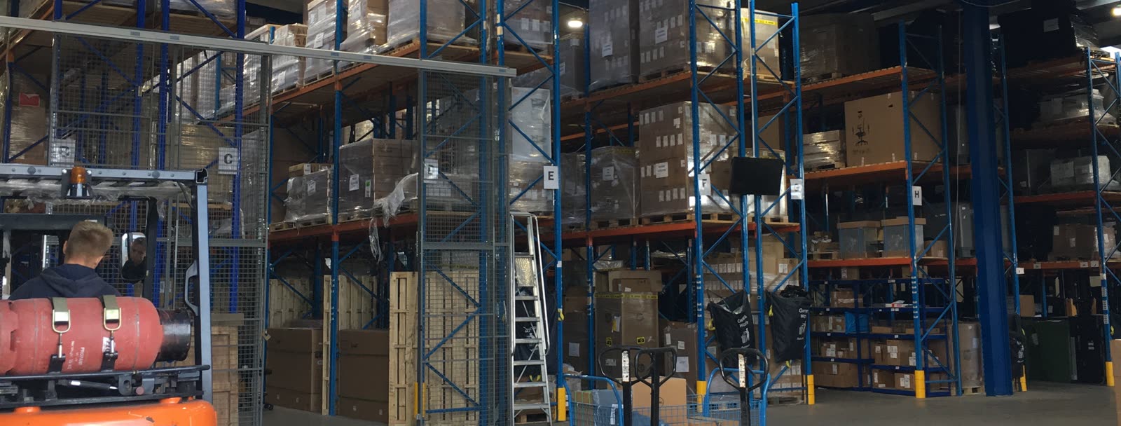 The warehouse floor, with palletised stock racked bay by bay and a forklift working the aisle